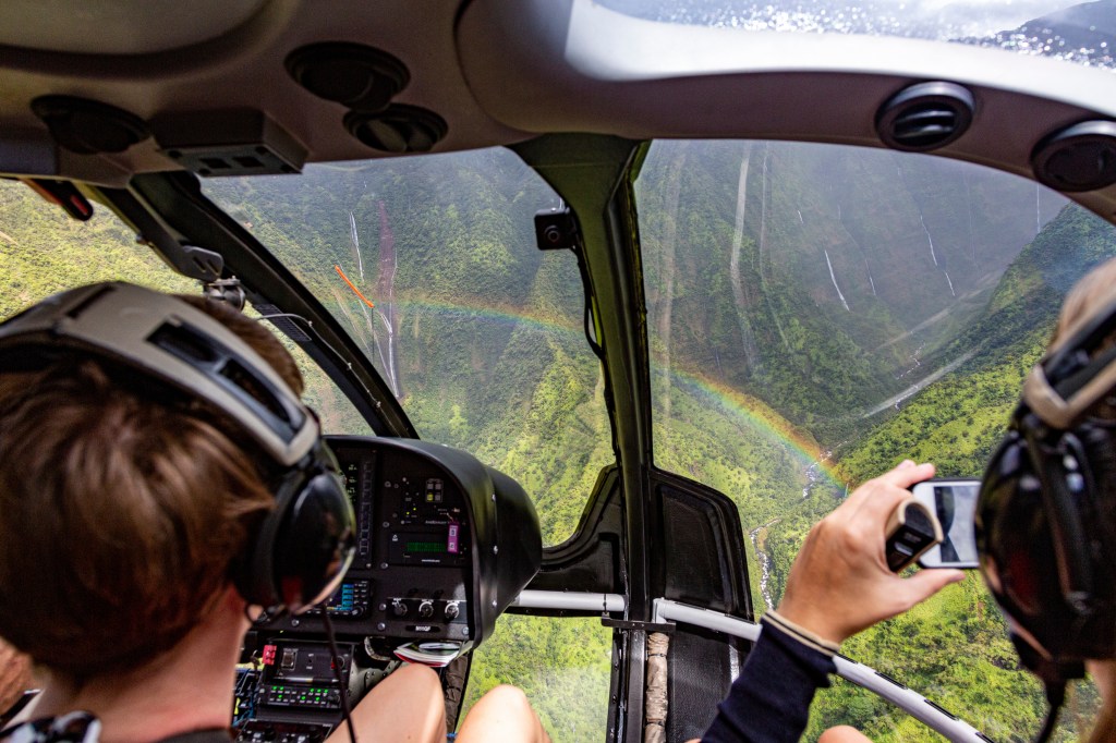 Two people on a helicopter tour in kauwai of waimea canyon looking at a rainbow